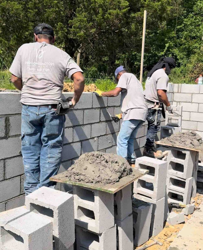 Construction workers actively laying concrete blocks for a new building's foundation, showing teamwork and construction expertise.