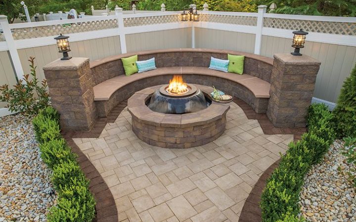 A cozy outdoor living area featuring a circular concrete fire pit, complemented by curved bench seating and paver flooring, ideal for residential landscape projects.
