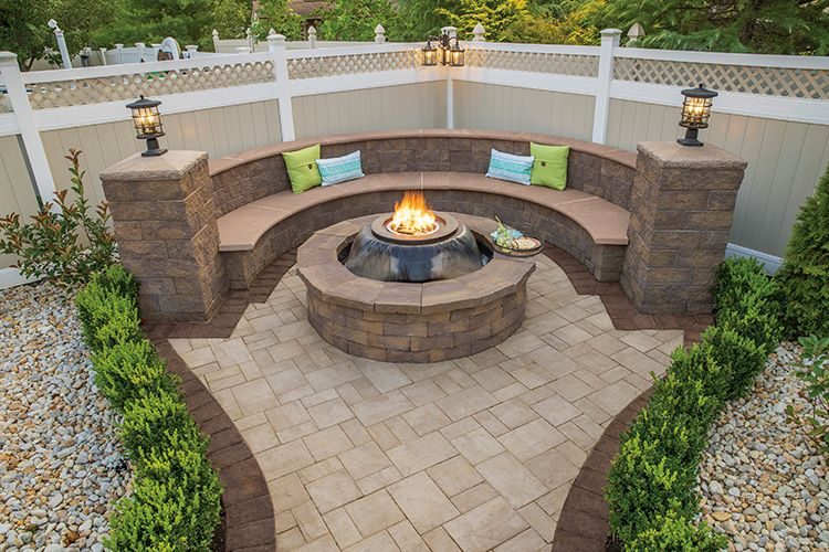 A cozy outdoor living area featuring a circular concrete fire pit, complemented by curved bench seating and paver flooring, ideal for residential landscape projects.