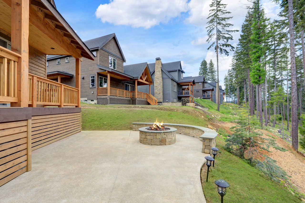 Rustic mountain home featuring an expansive concrete patio with a central fire pit, bordered by wooded areas, ideal for outdoor gatherings.