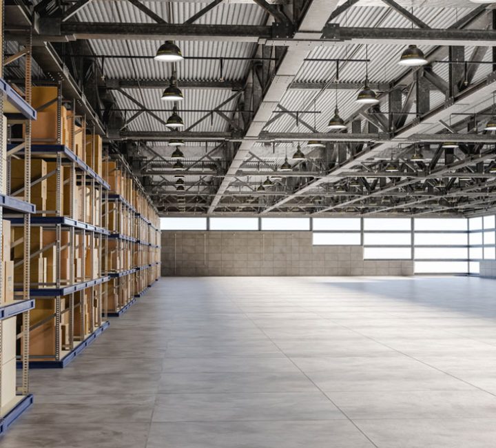 The interior of a spacious warehouse with high ceilings, metal shelving units filled with boxes, and ample natural light streaming through large windows.